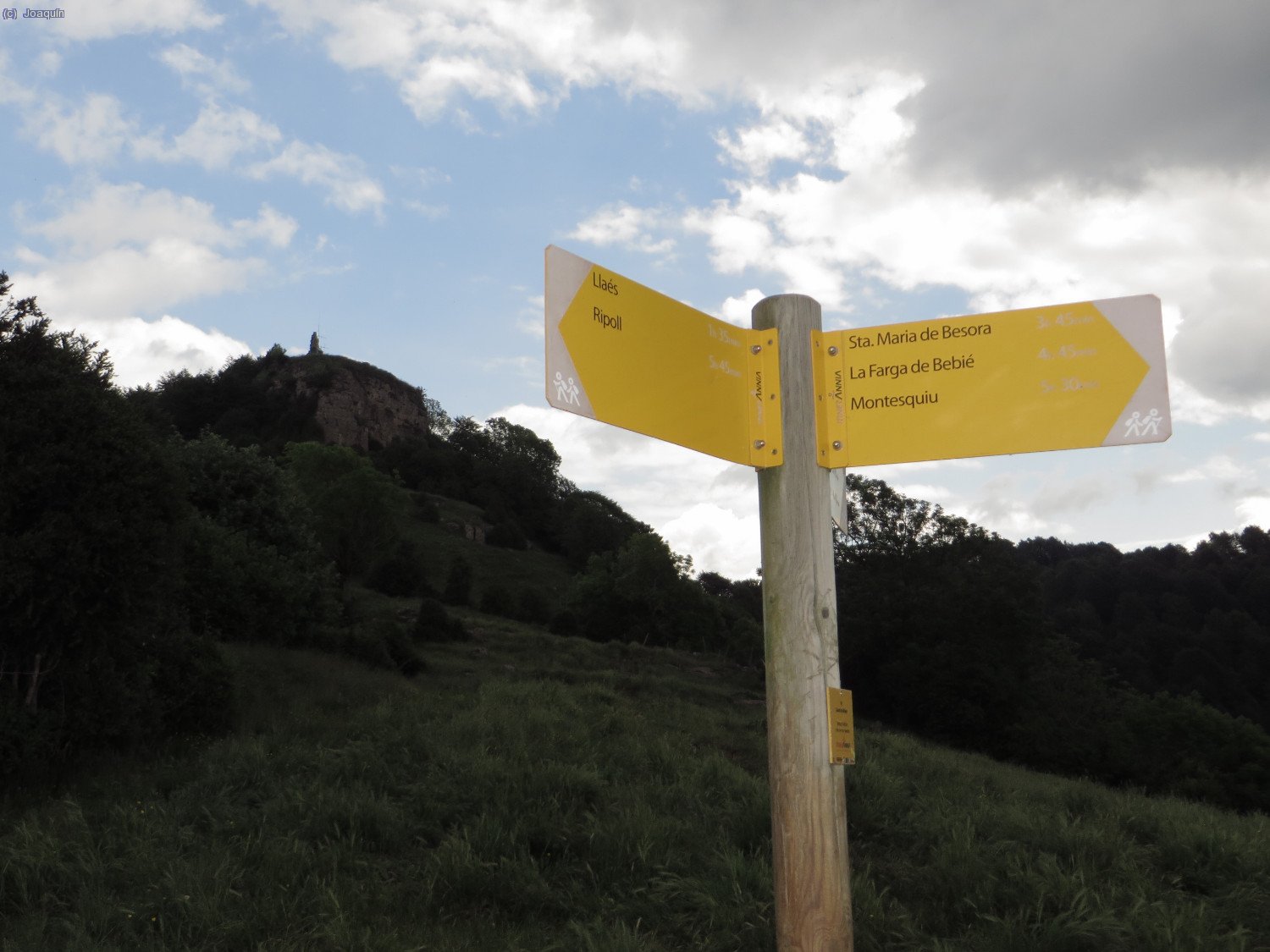 Cartel indicador de recorridos, detrás el Castell de Milany
