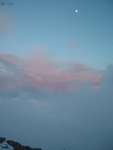 La lluna gronxan-se sobre un bre&ccedil;ol de n&uacute;vols rosats pel sol. Capvespre als Alps.